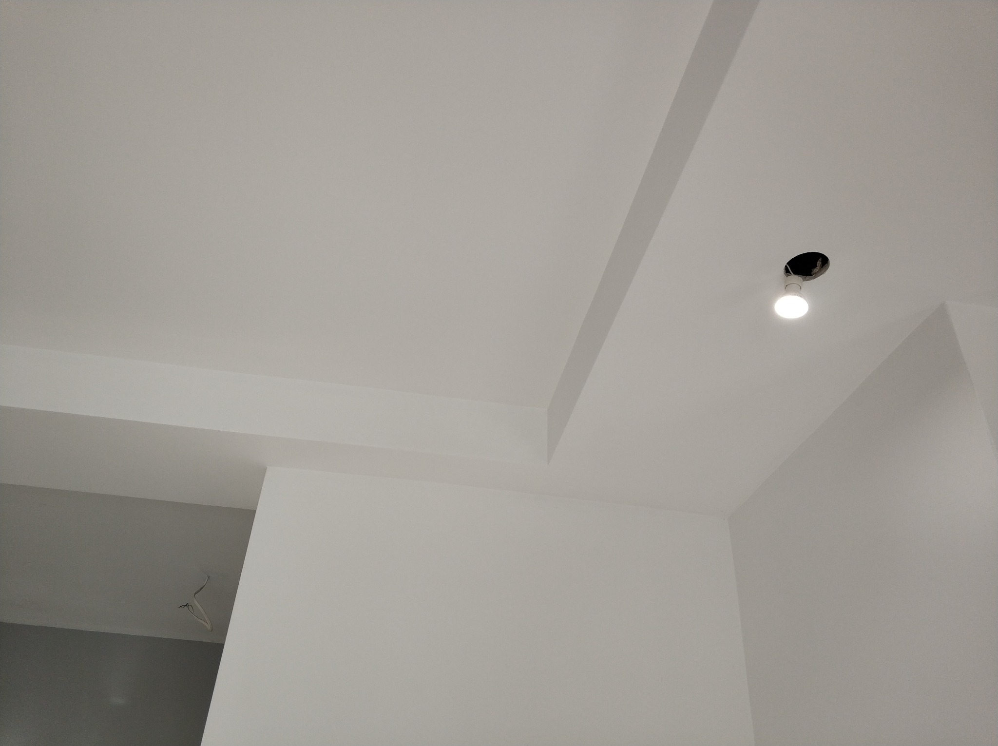 Gładka, biała powierzchnia sufitu z widoczną wnęką i zamontowanym oświetleniem punktowym; widoczne fragmenty ścian w tym samym kolorze.