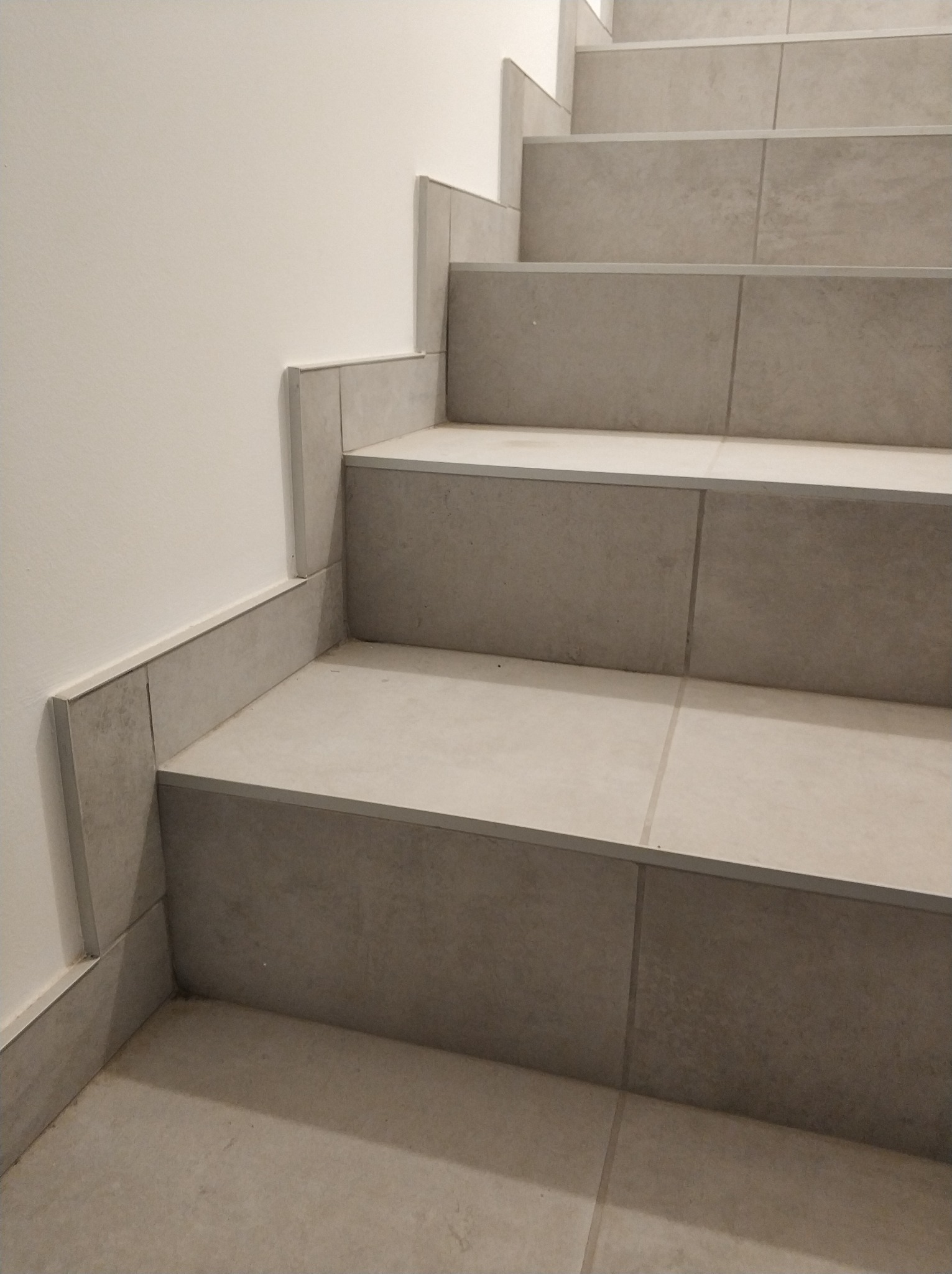 Schody wyłożone szarymi płytkami ceramicznymi, widok z dołu, minimalistyczny design.