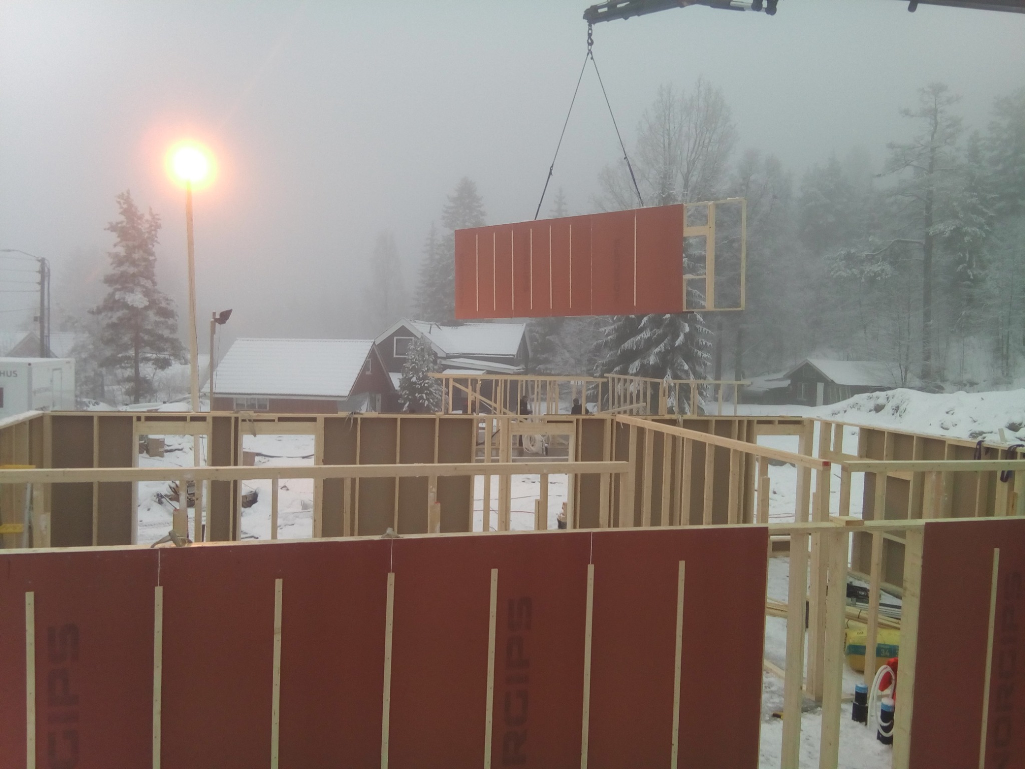 Montaż ściany szkieletowej domu w Olkuszu, widok na konstrukcję z drewnianych belek i czerwoną płytę, w tle zimowy krajobraz i mgła.