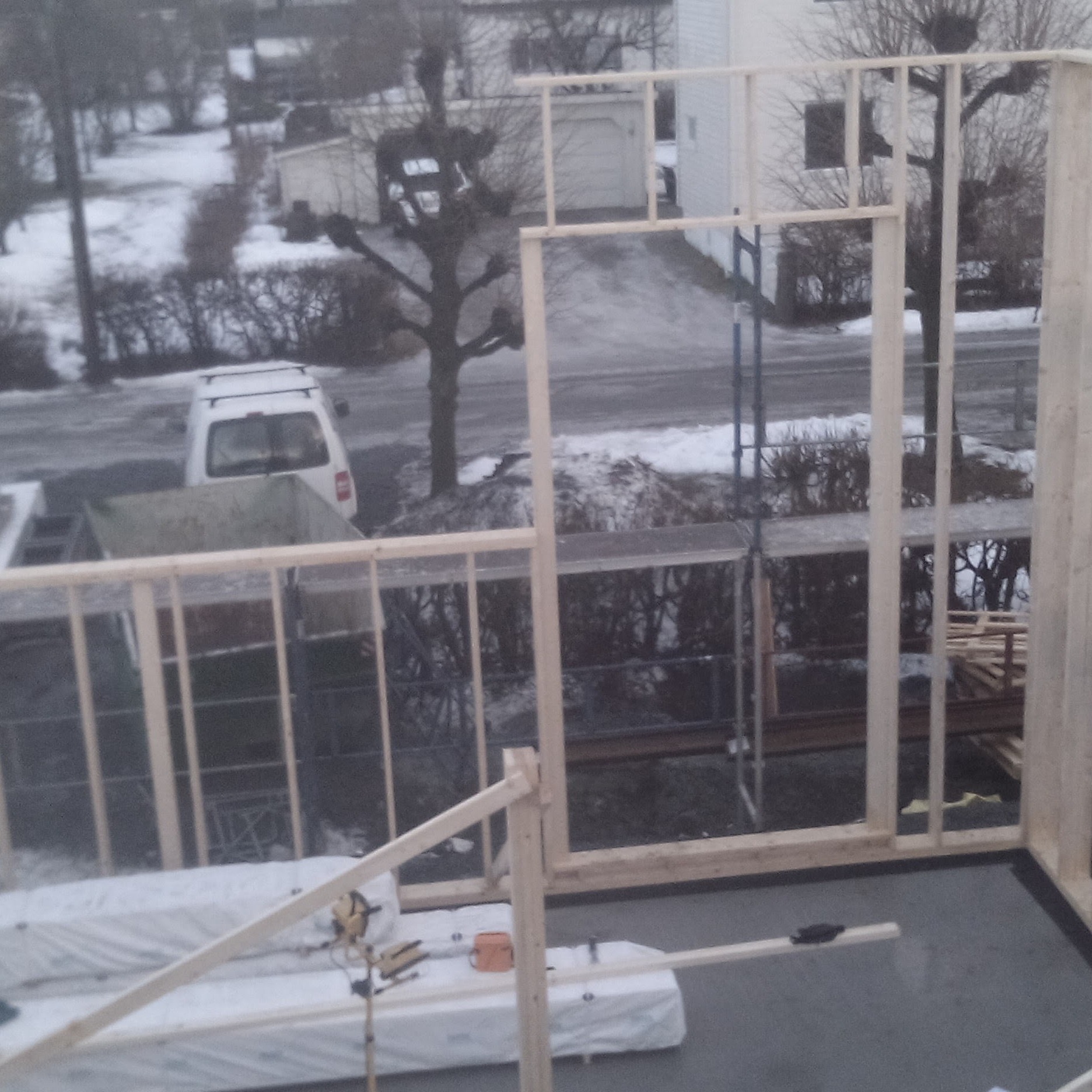 Wznoszenie drewnianej konstrukcji szkieletowej domu w zimowej scenerii; widoczne elementy konstrukcyjne, narzędzia i materiały budowlane na tle ośnieżonego krajobrazu.