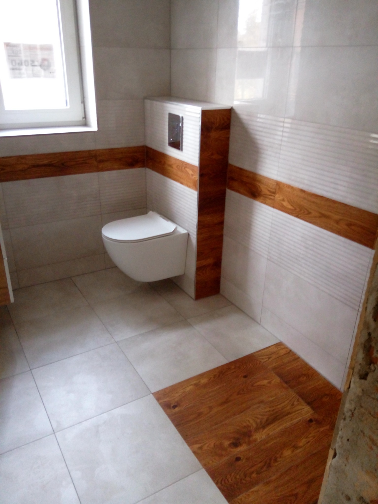 Nowoczesna łazienka z podwieszaną toaletą, białymi płytkami z poziomymi paskami i drewnopodobnymi akcentami na ścianach i podłodze.