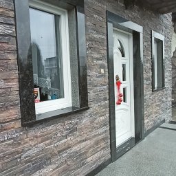Kamieniarstwo Szymański Wojciech - Elewacja budynku z kamienia dekoracyjnego, okna i drzwi obramowane czarnym granitem. Parapet z granitu. Schody wejściowe wyłożone kamieniem. Dekoracja świąteczna na drzwiach.