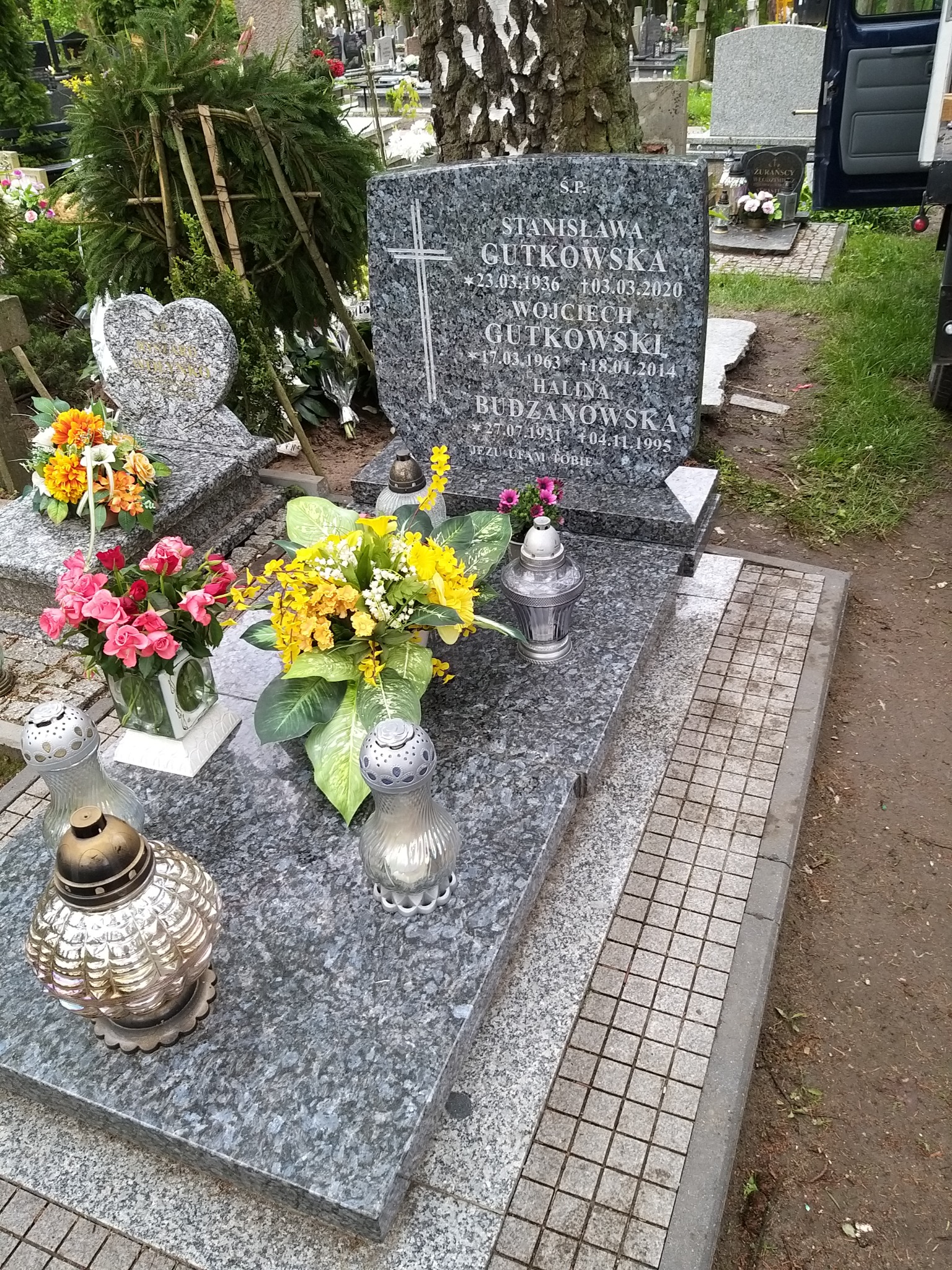 Granitowy pomnik z wygrawerowanymi danymi zmarłych, ozdobiony świeżymi kwiatami i lampionami, na cmentarzu w Łosinie.