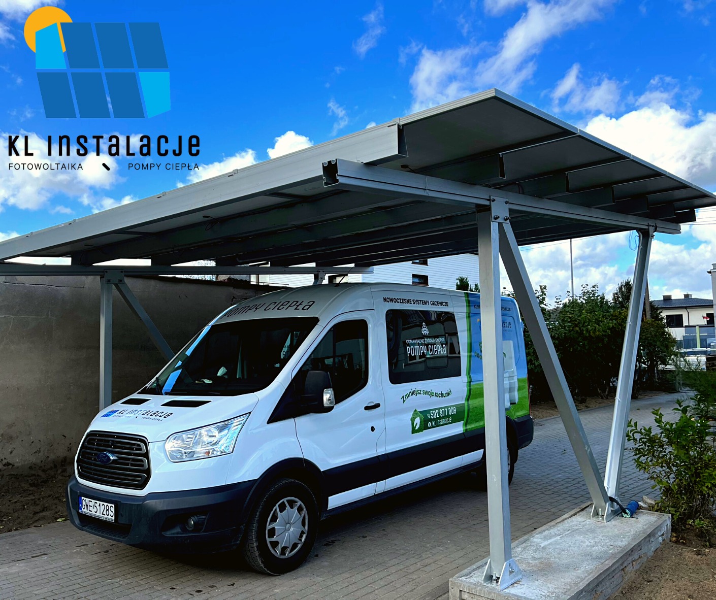 Instalacja fotowoltaiczna na konstrukcji carport, z białym busem firmy instalacyjnej zaparkowanym pod spodem, widoczne panele słoneczne i logo firmy na pojeździe.
