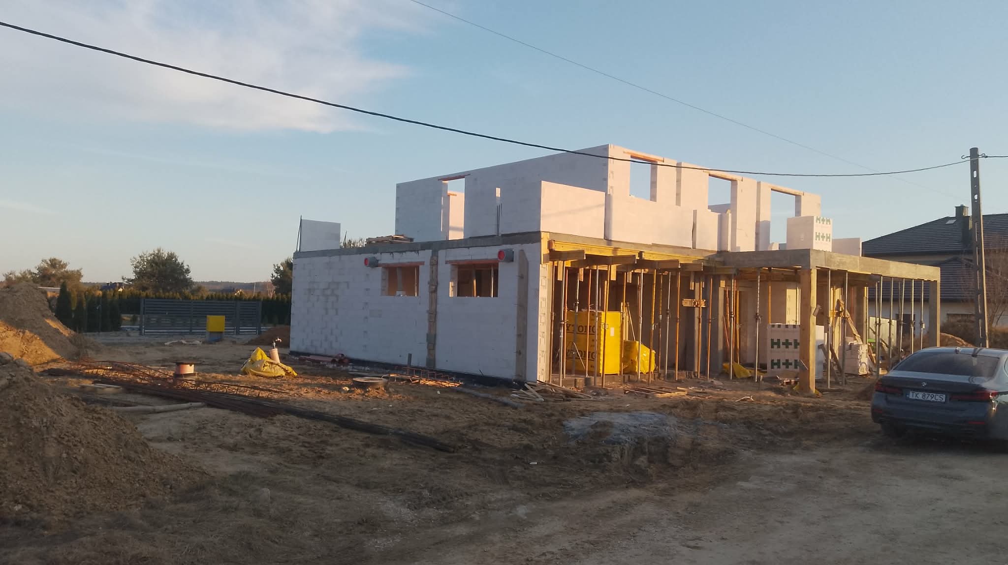 Budowa domu z betonu komórkowego: ściany parteru i szalunek stropu w trakcie realizacji. Widoczne bloczki H+H, teren budowy i zaparkowany samochód osobowy.