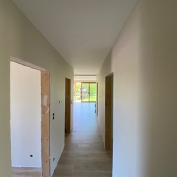Prestige House Tomasz Caputa p - Korytarz po remoncie: świeżo pomalowane ściany w odcieniach beżu, drewnopodobna podłoga z płytek, surowe ościeżnice drzwiowe czekają na montaż.