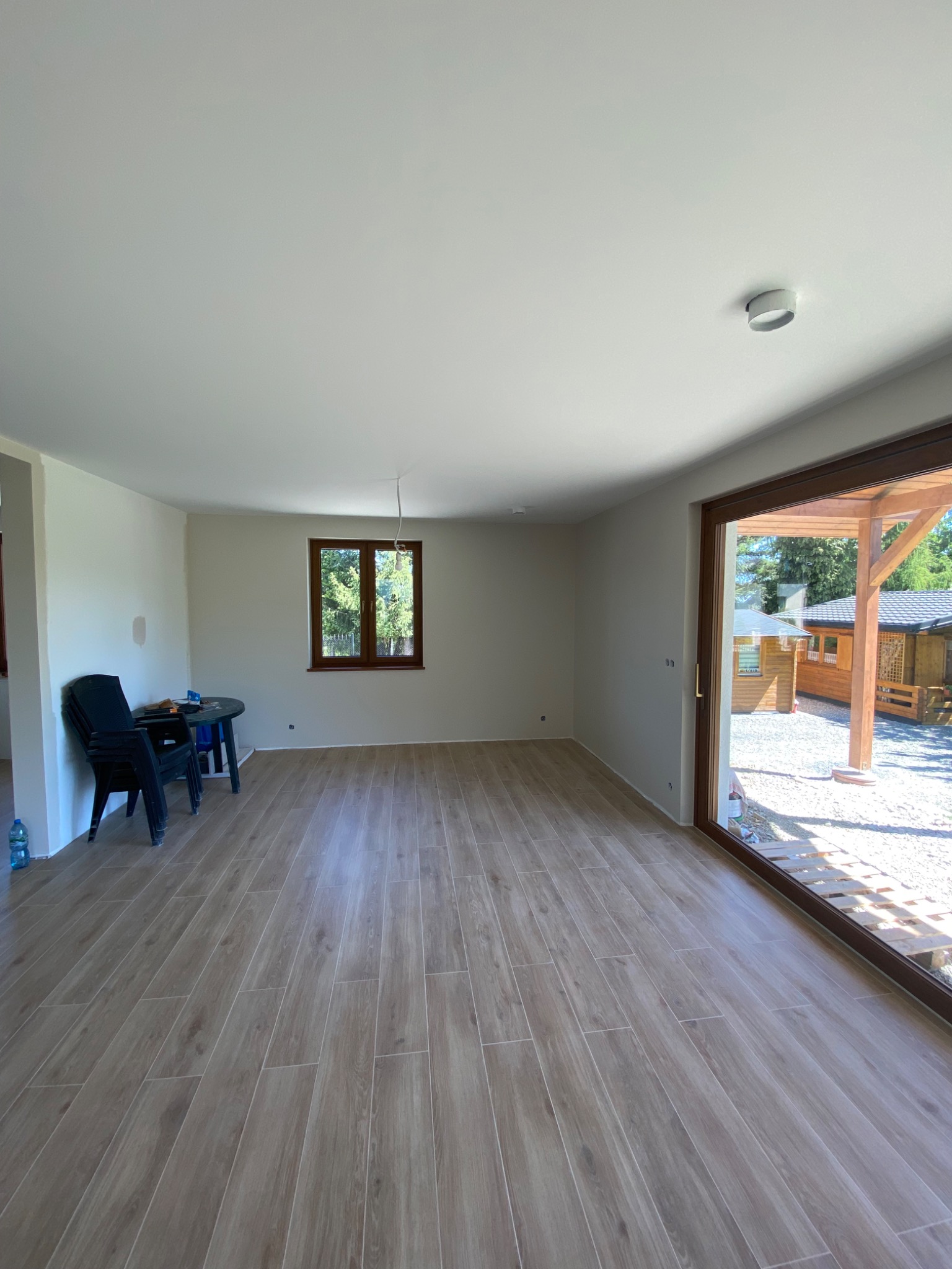 Jasne wnętrze po remoncie: świeżo pomalowane ściany, drewnopodobne płytki na podłodze, duże okno z widokiem na zewnątrz. Minimalistyczny wystrój.