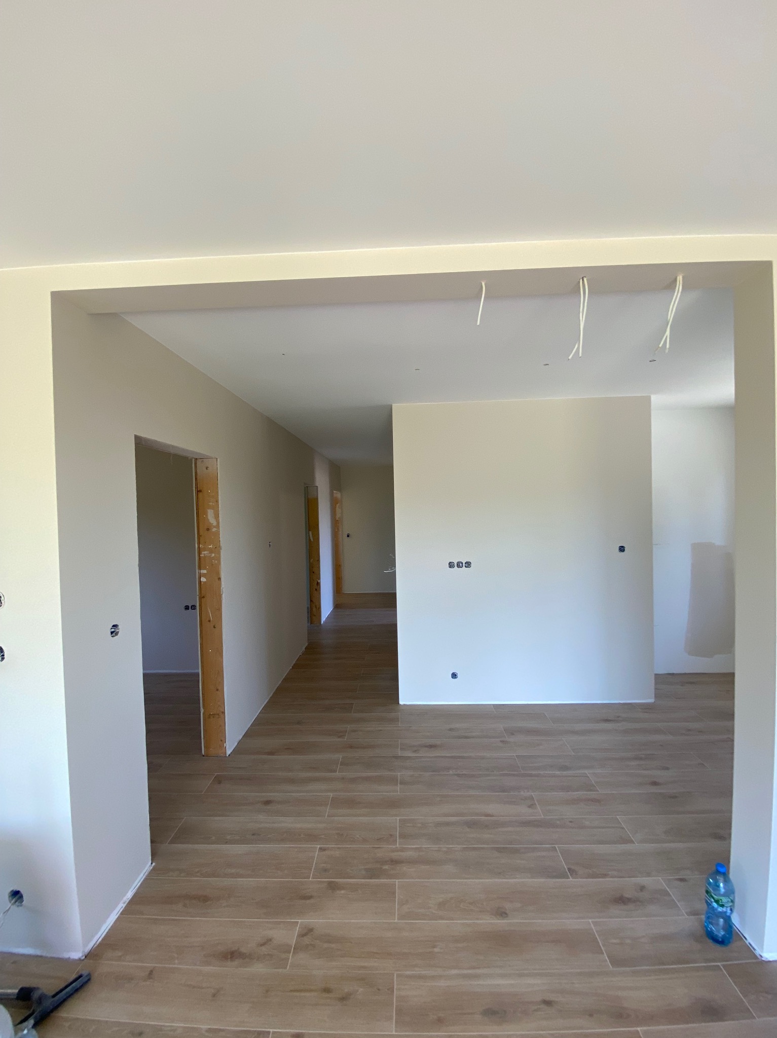 Jasne wnętrze w trakcie prac wykończeniowych: świeżo położona podłoga z paneli imitujących drewno, pomalowane ściany, widoczne kable i narzędzia.