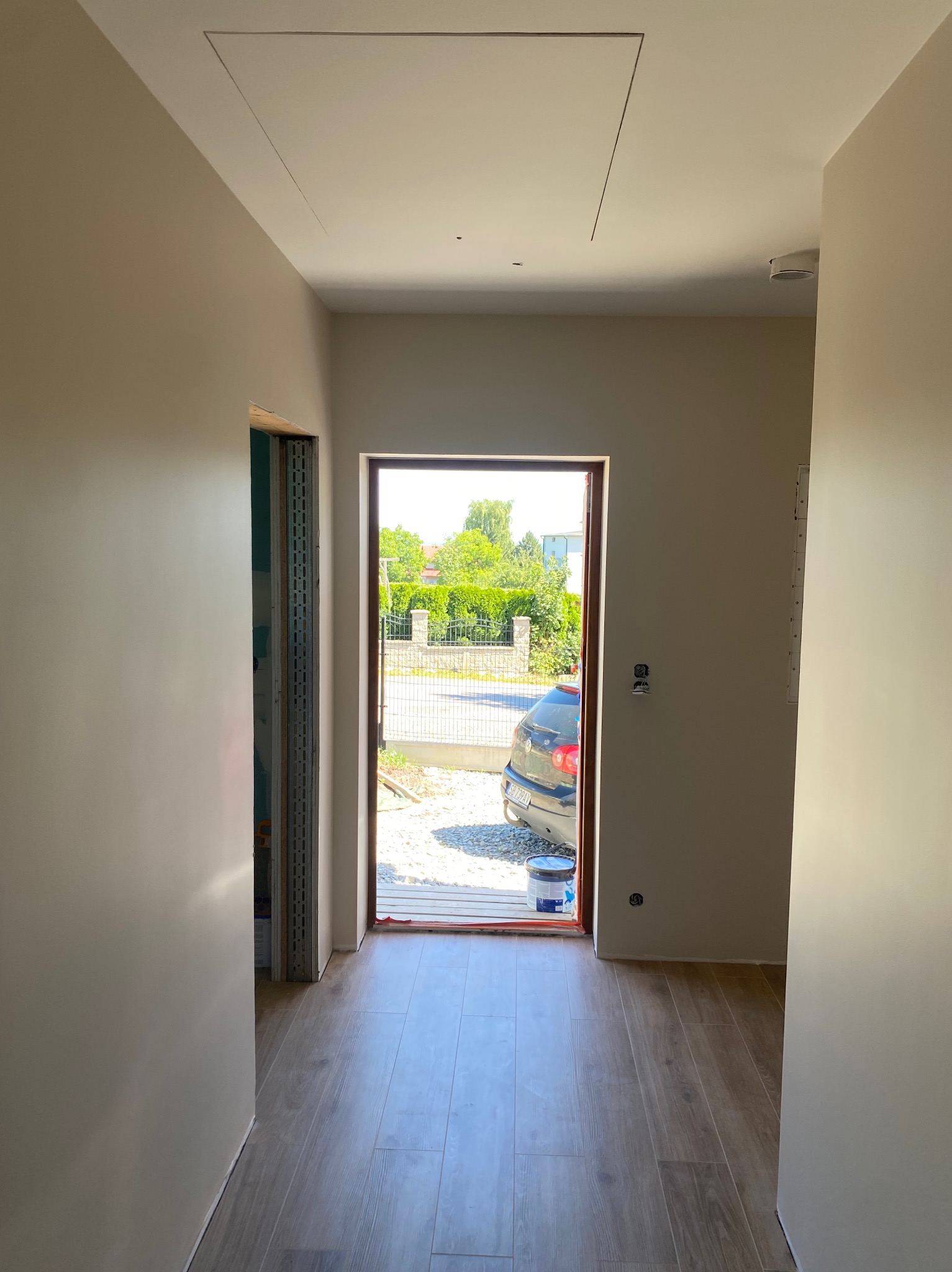 Wnętrze korytarza po malowaniu ścian na jasny odcień. Widoczna podłoga z paneli imitujących drewno, drzwi wejściowe i klapa rewizyjna w suficie.