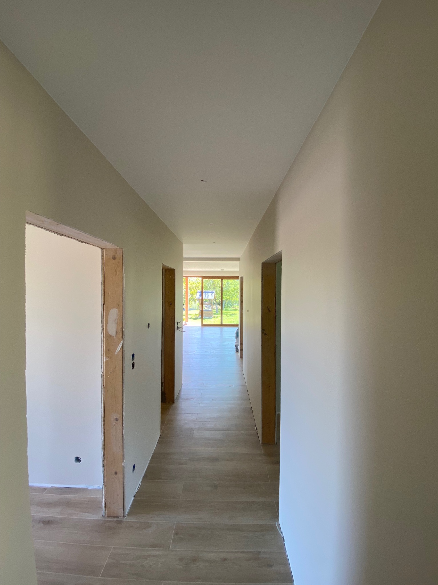 Korytarz w trakcie wykańczania w Bielsko-Białej. Widoczne świeżo pomalowane ściany w odcieniach beżu i ułożona podłoga z płytek imitujących drewno. Ościeżnice drzwiowe surowe.