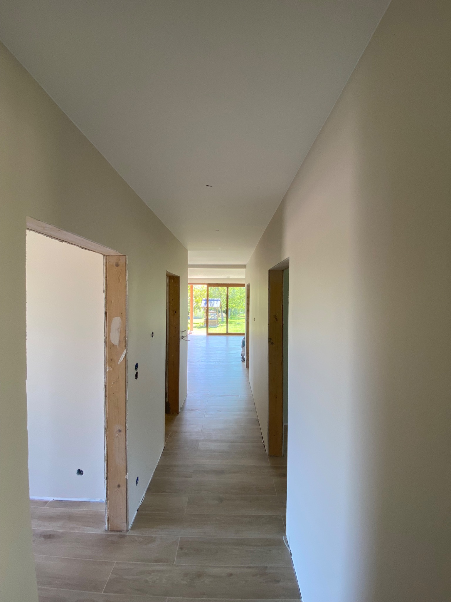 Korytarz po remoncie: świeżo pomalowane ściany w odcieniach beżu, drewnopodobna podłoga z płytek, surowe ościeżnice drzwiowe czekają na montaż.