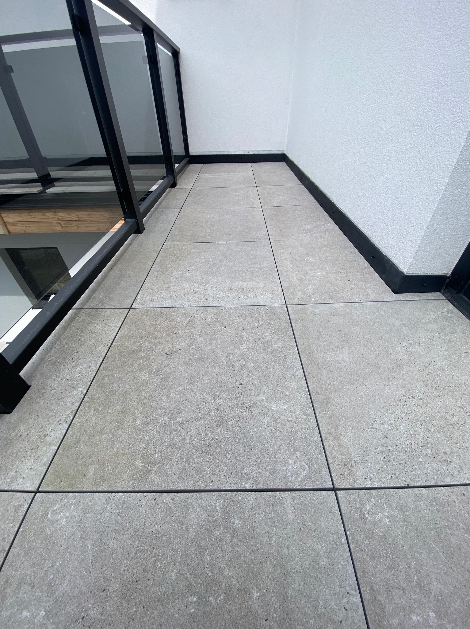 Wykończony balkon w Bielsku-Białej z szarymi płytkami i czarną balustradą. Minimalistyczny design, widok z góry. Precyzyjnie ułożona podłoga.