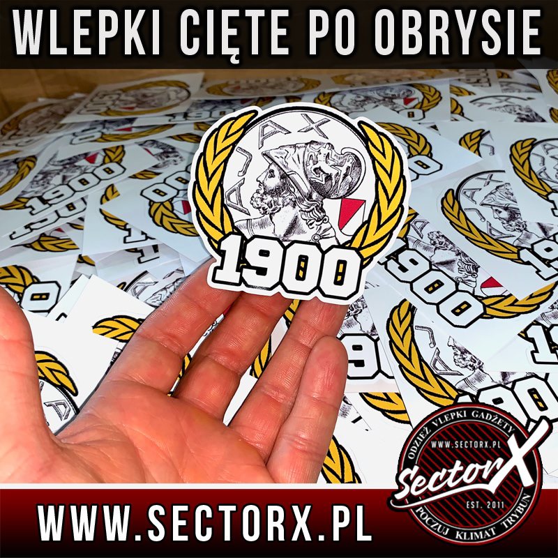 Ręka trzyma naklejkę foliową z grafiką przedstawiającą głowę mężczyzny w wieńcu laurowym i rokiem 1900, wyciętą po obrysie, na tle innych podobnych naklejek.