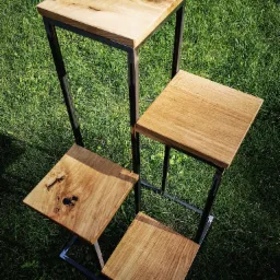 Czteropoziomowy kwietnik w stylu loft z drewnianymi blatami o zróżnicowanej strukturze i metalowym stelażem, ustawiony na trawie.