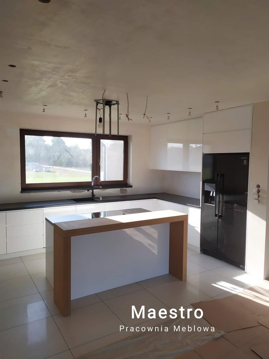 Nowoczesna, jasna kuchnia z wyspą w Kielcach, jeszcze w trakcie wykańczania - widoczne niedokończone podłączenia oświetlenia sufitowego.