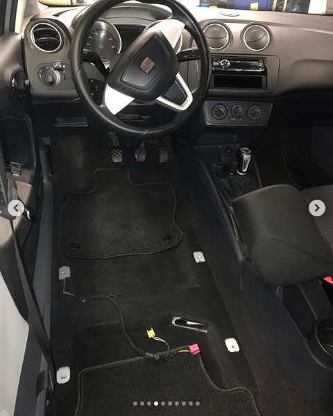 Wnętrze samochodu marki Seat z widoczną deską rozdzielczą, kierownicą i podłogą, na której widoczne są odpięte przewody elektryczne w kolorach żółtym i czerwonym, sugerujące demontaż elementów...