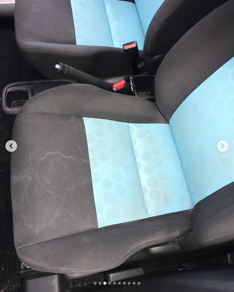 Brudny fotel samochodowy z czarną tapicerką i jasnoniebieskim pasem z wzorem w kółka, widoczne plamy i zabrudzenia na materiale.