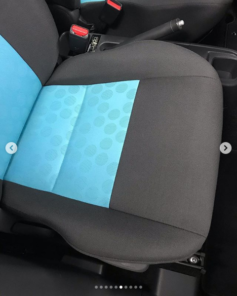 Szczegółowe ujęcie fotela samochodowego z czarną tapicerką i turkusowymi wstawkami w kropki, widoczny hamulec ręczny i fragment pasów bezpieczeństwa.