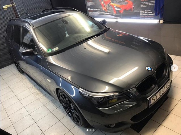 Błyszczący, grafitowy samochód kombi BMW serii 5 po detailingu, widoczny z góry w jasnym oświetleniu warsztatowym, z czarnymi felgami i tablicą rejestracyjną SY 8814K.