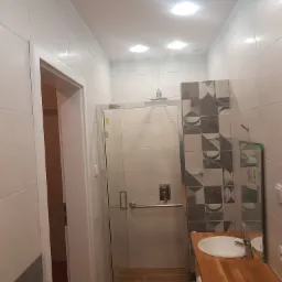 Nowoczesna łazienka z kabiną prysznicową typu walk-in, umywalką nablatową na drewnianym blacie i płytkami w geometryczne wzory na ścianie.