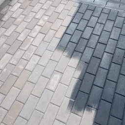 Czyszczenie kostki brukowej: widoczna różnica między wyczyszczoną, mokrą, ciemnoszarą częścią a suchą, jasnoszarą częścią. Ślady czyszczenia widoczne na granicy.