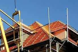 Konstrukcja dachu w trakcie budowy, widoczne krokwie, łaty i kontrłaty, rusztowanie w kolorze żółtym i srebrnym, błękitne niebo w tle.