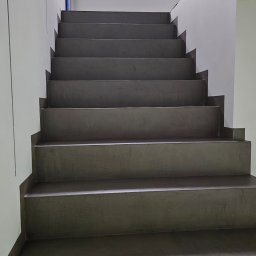 MiP RESIN - Schody wykończone szarą posadzką. Widoczne stopnie i fragment okna na górze. Minimalistyczny design, gładka powierzchnia, jednolite wykończenie.