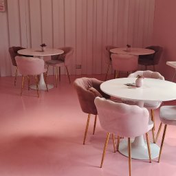 MiP RESIN - Różowa posadzka żywiczna w kawiarni z welurowymi krzesłami i białymi stolikami. Widoczny fragment lady chłodniczej i okno z dekoracją.