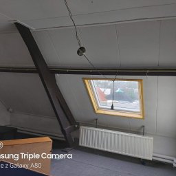 MMM Montage - Poddasze ze skośnym sufitem wykończonym panelami, widoczne okno dachowe, grzejnik i elementy instalacji elektrycznej. Ukończone prace wykończeniowe.