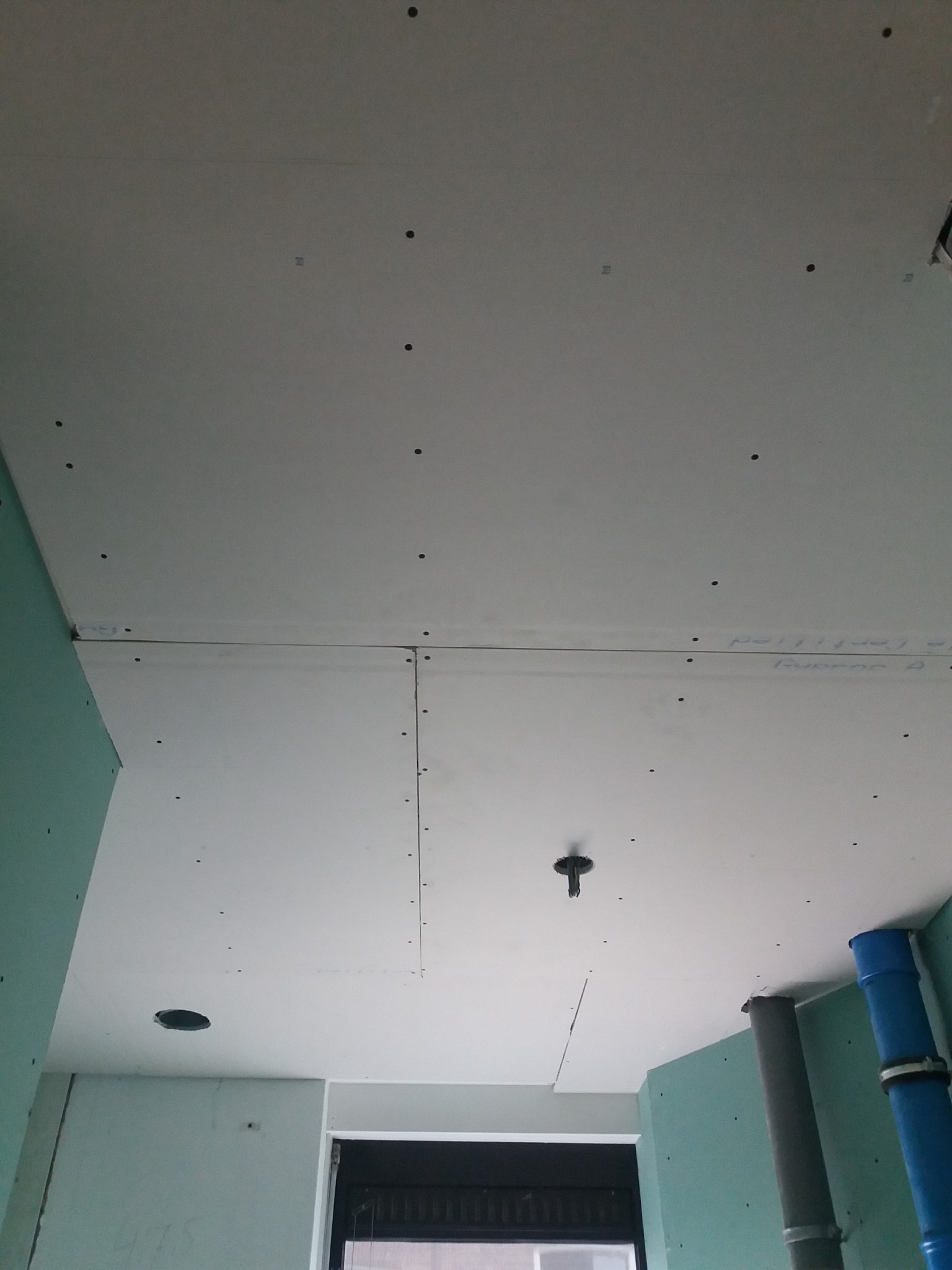 Montaż sufitu podwieszanego z płyt gipsowo-kartonowych, widoczne profile, otwór na oświetlenie i instalacje wentylacyjne.