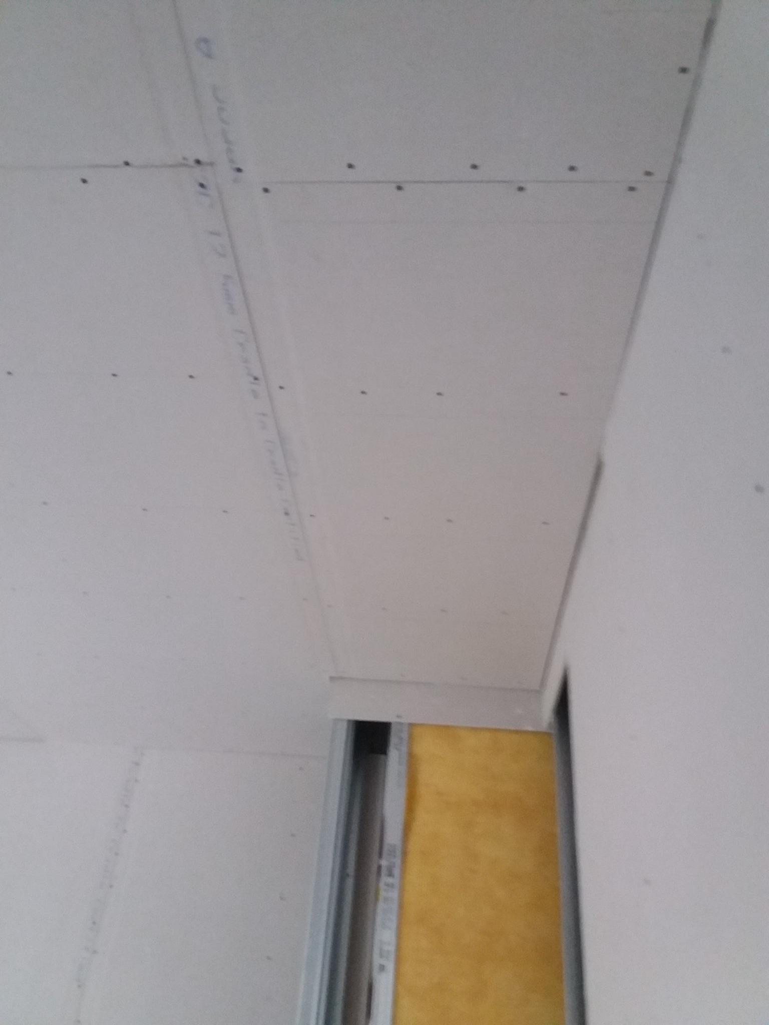 Montaż sufitu podwieszanego z widoczną konstrukcją metalową, izolacją z wełny mineralnej oraz płytami, częściowo przymocowanymi wkrętami.