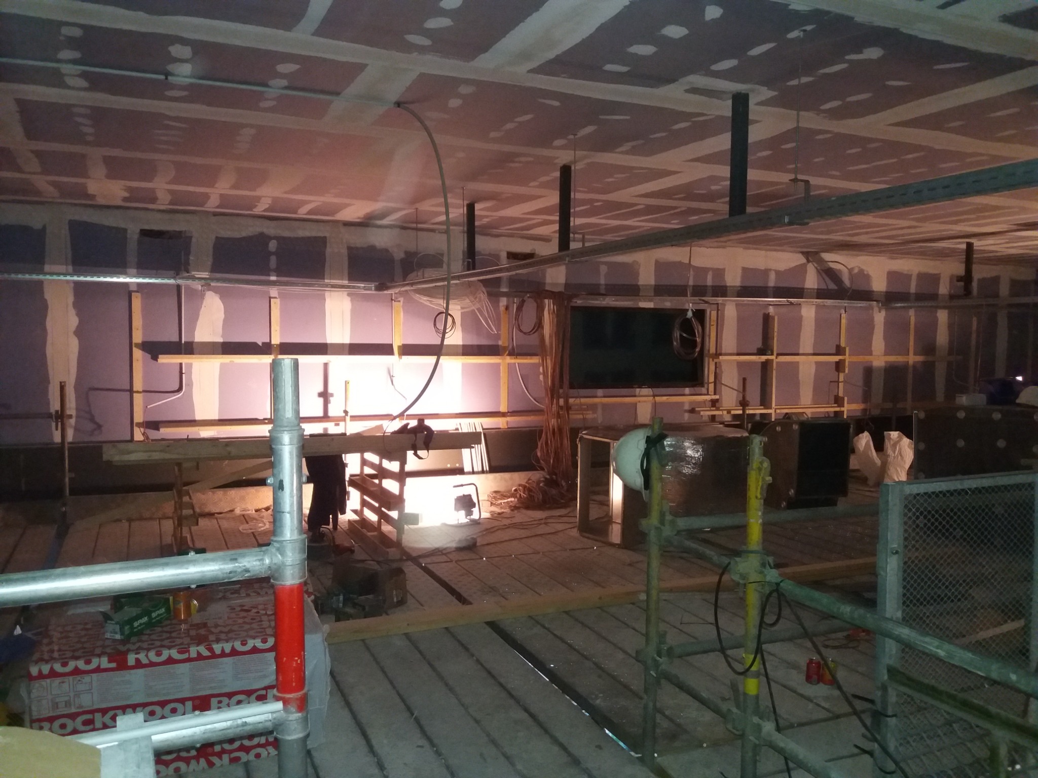 Wnętrze w trakcie prac wykończeniowych: sufit z płyt gipsowo-kartonowych z widocznymi łączeniami, rusztowania, materiały izolacyjne Wool Rockwood i instalacje elektryczne.