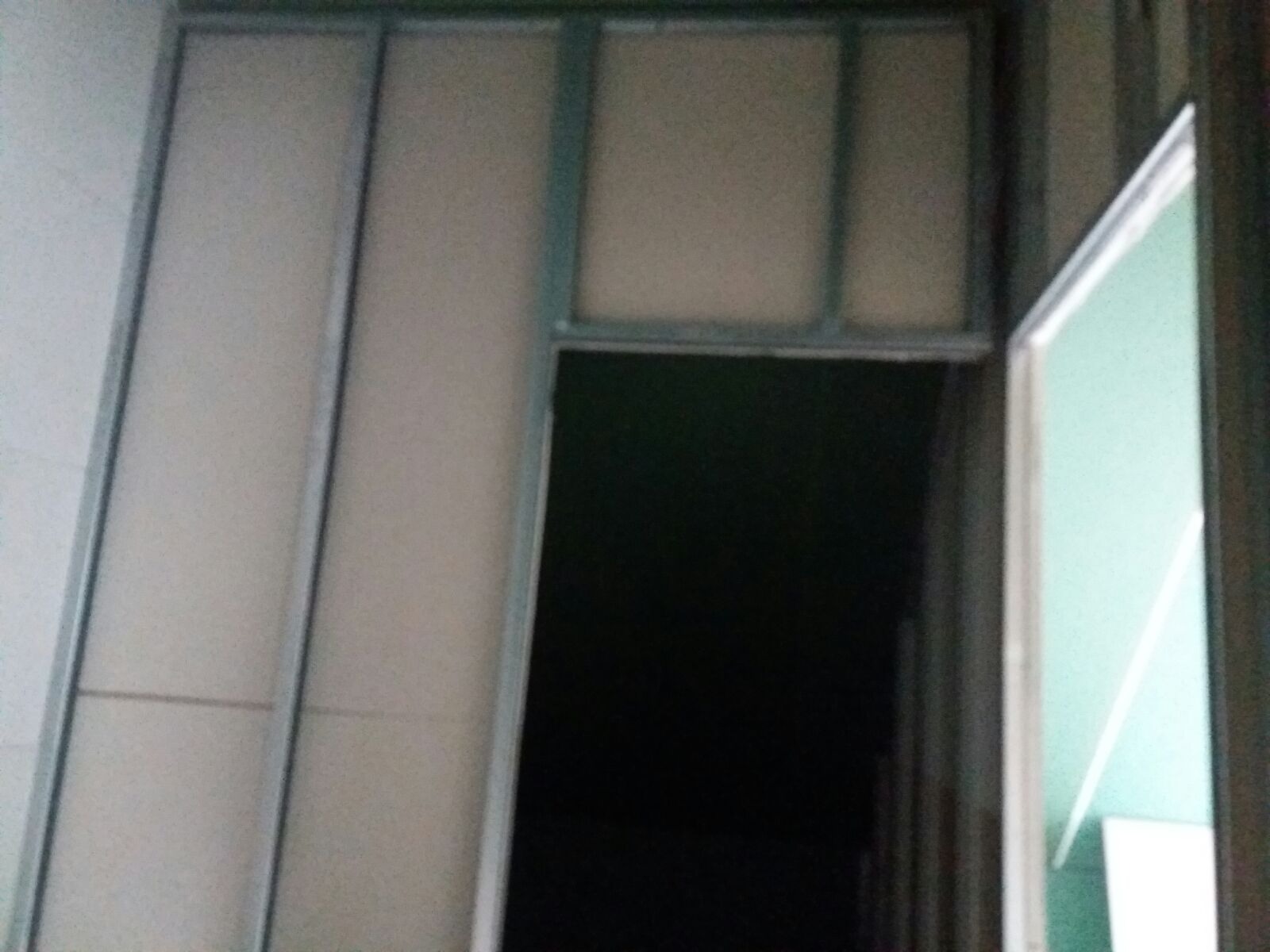 Montaż ścianki działowej z profili i płyt. Widoczne metalowe profile i fragment płyty, z otworem drzwiowym po prawej stronie.