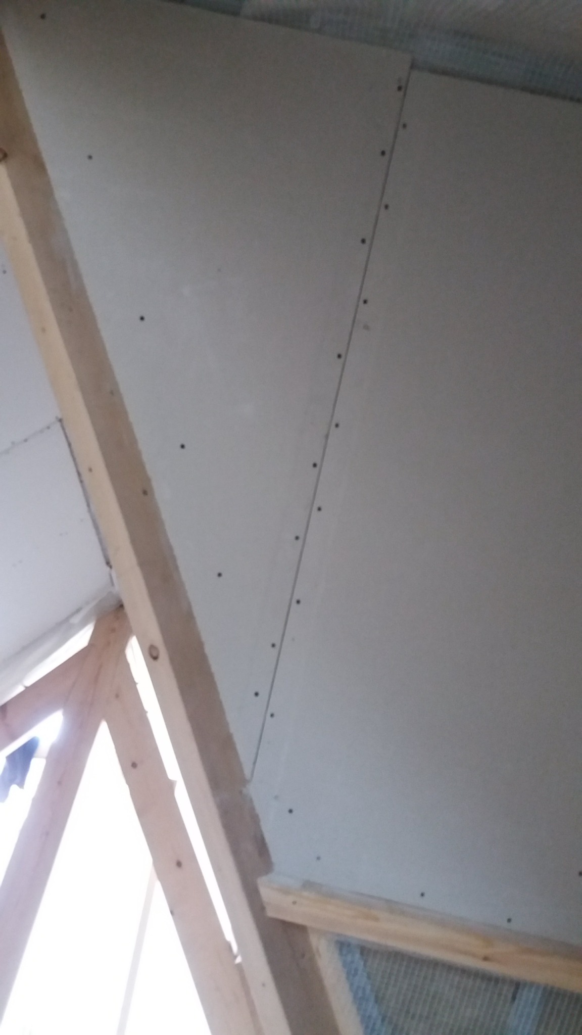 Montaż płyty karton gips na skośnym suficie poddasza, widoczne drewniane elementy konstrukcyjne i wkręty mocujące.