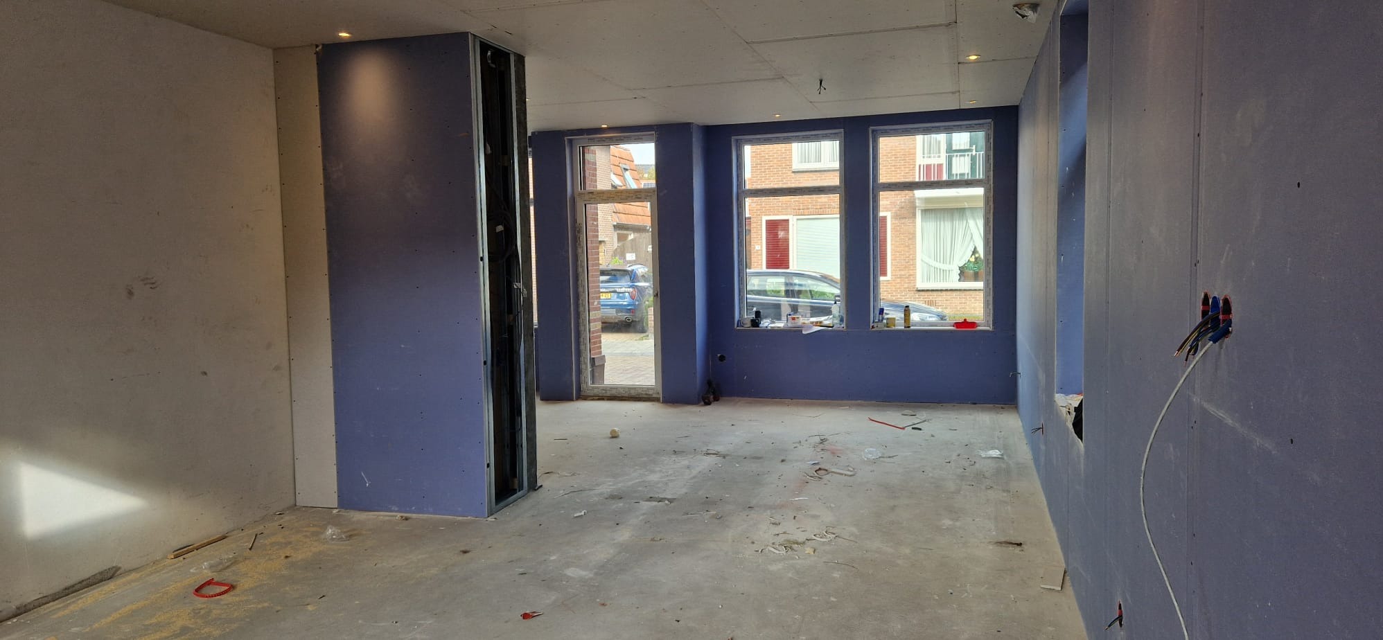 Pokój w trakcie prac wykończeniowych: ściany z płyt kartonowo-gipsowych w kolorze fioletowym, widoczne kable elektryczne, okna z widokiem na ulicę.