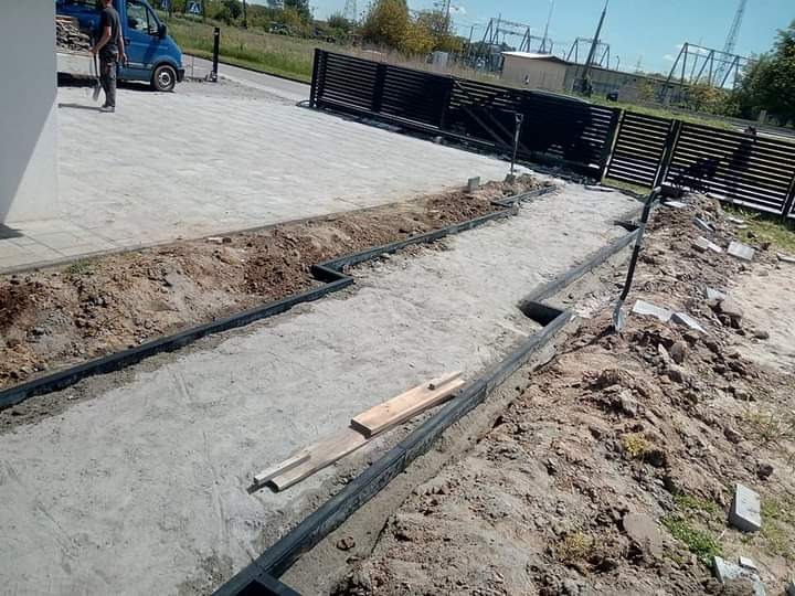 Przygotowanie podłoża pod kostkę brukową z zamontowanym drenażem liniowym, widoczne obrzeża i piasek stabilizujący.