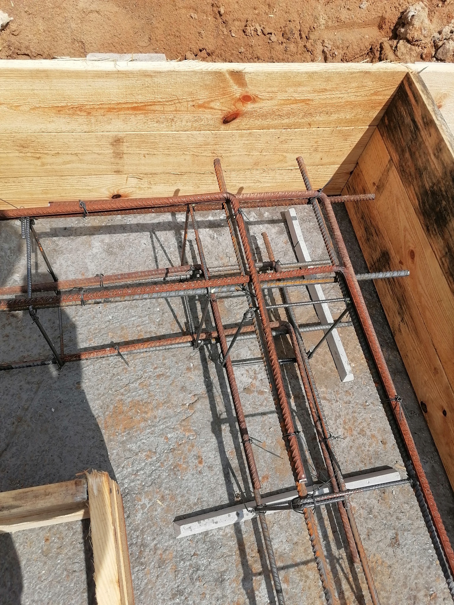 Zbrojenie fundamentów z prętów stalowych połączonych drutem, umieszczone w drewnianym szalunku, z dystansami betonowymi, przygotowane do zalania betonem.