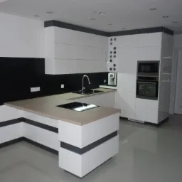 Nowoczesna kuchnia z białymi szafkami i blatem w odcieniach drewna, czarny panel nad blatem, wyspa kuchenna z płytą indukcyjną, oświetlenie punktowe, widoczny ekspres do kawy.