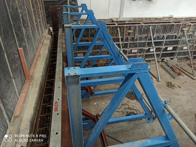 Szczegółowe ujęcie szalunków fundamentowych z widocznym zbrojeniem i niebieskimi podporami, przygotowanych do zalewania betonem.