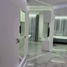 Nowoczesne wnętrze mieszkania z białymi meblami, marmurową podłogą i oświetleniem LED wzdłuż sufitu i podłogi, widok zza uchylonych drzwi.