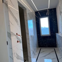 Oleh Tanchak Top Remont - Nowoczesna łazienka z marmurowymi płytkami w odcieniach bieli i czerni, podświetlanym sufitem i oknem. Widoczne niedokończone instalacje elektryczne.