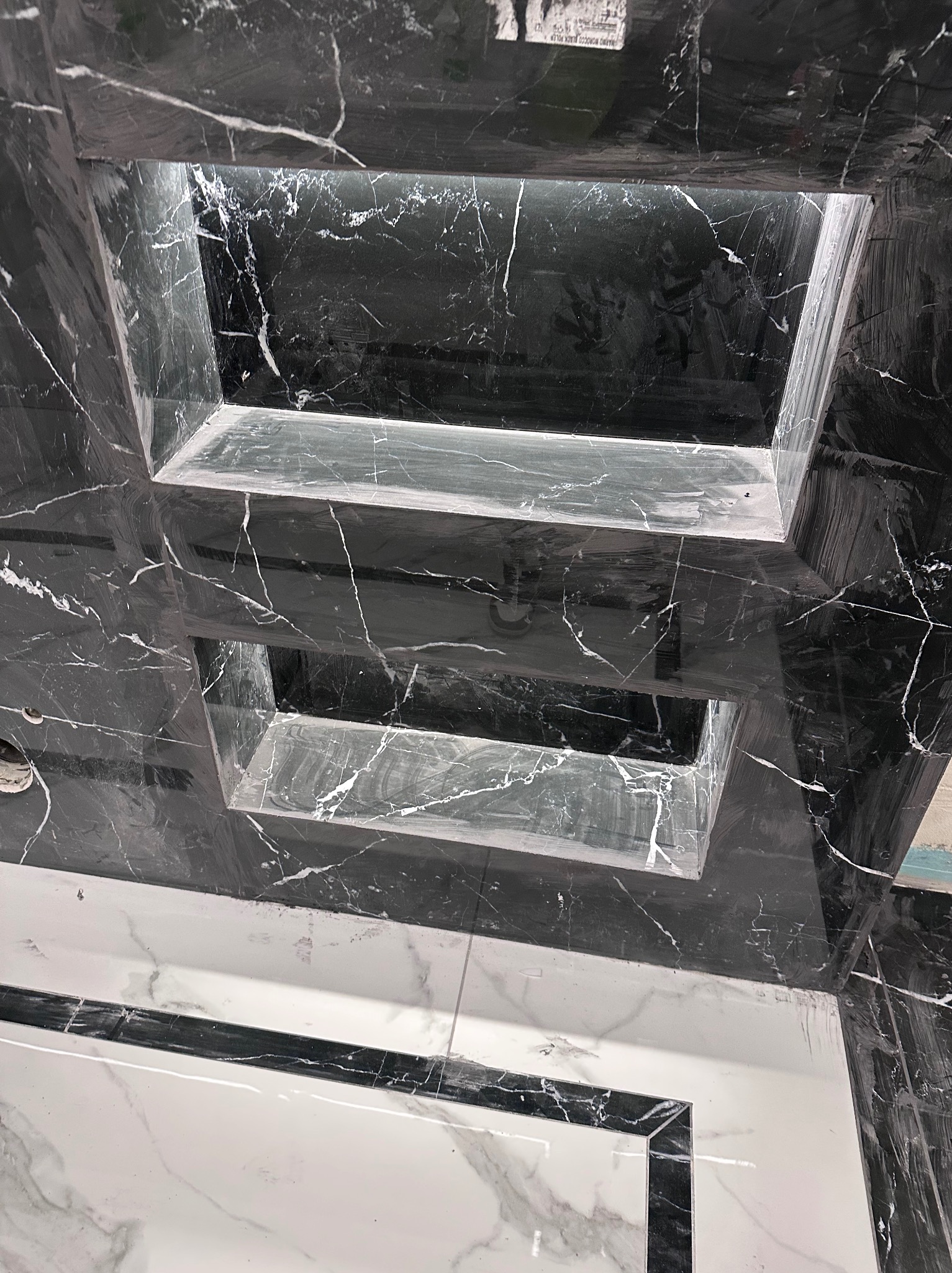 Czarno-biała marmurowa ściana z wnękami oświetlonymi od wewnątrz, widok z dołu, podkreślający unikalny wzór kamienia i precyzję wykonania.