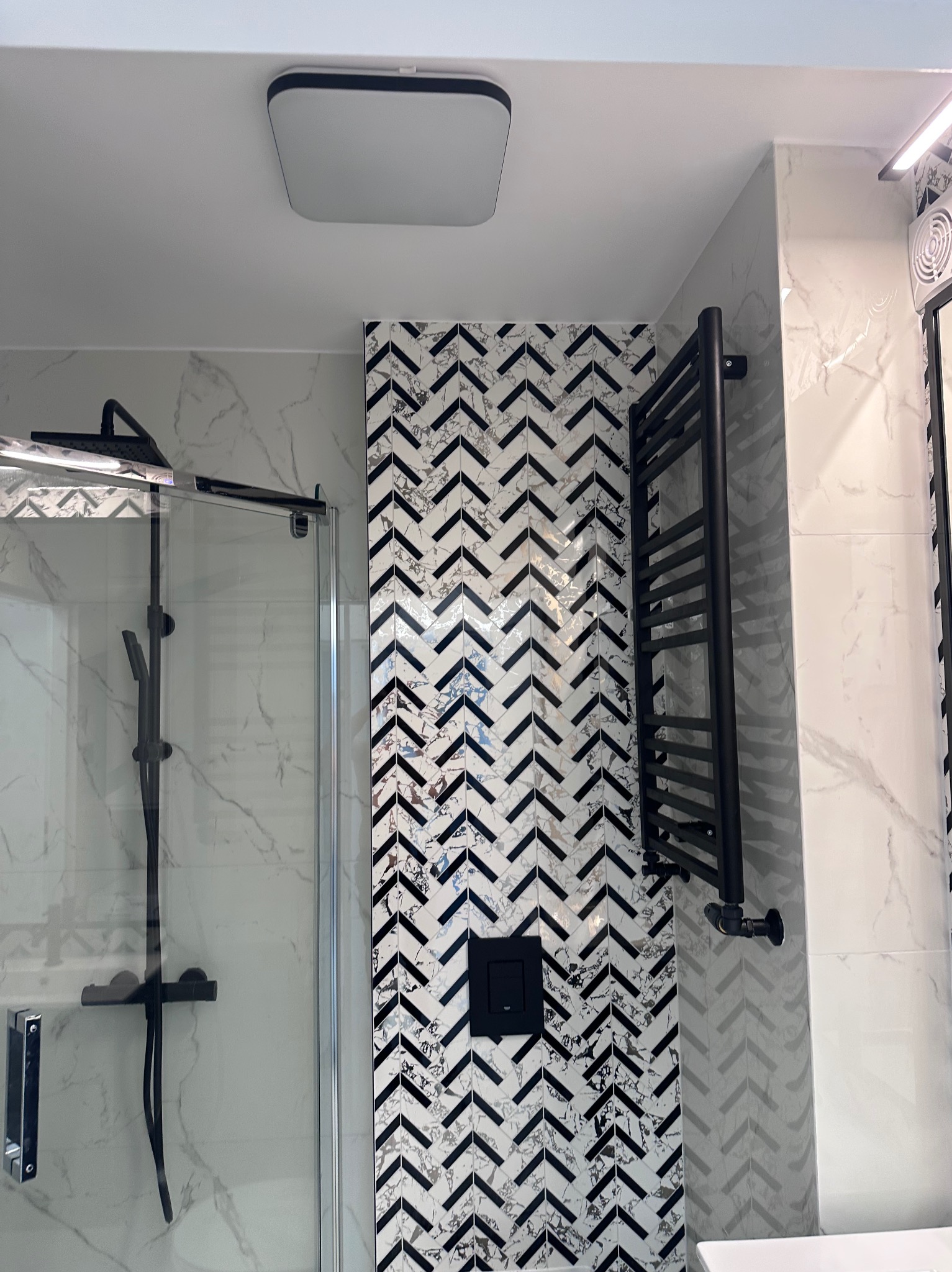 Nowoczesna łazienka z kabiną prysznicową, czarnym grzejnikiem drabinkowym i mozaiką w jodełkę. Marmurowe płytki na ścianach, minimalistyczna armatura.