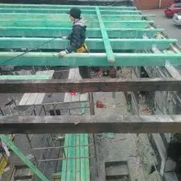 Pracownik w trakcie demontażu starej konstrukcji dachu, widoczne elementy więźby dachowej i fragmenty usuniętego pokrycia. Ujęcie z góry, w tle budynki i samochody.