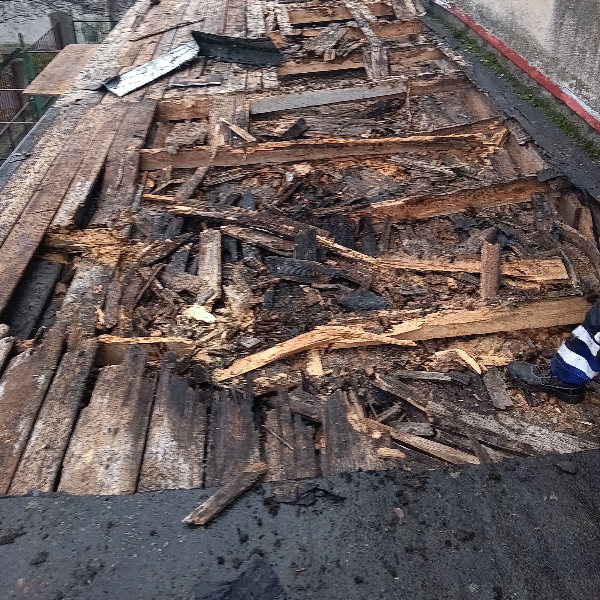 Uszkodzona konstrukcja dachu z widocznymi fragmentami desek i połamanych elementów, częściowo zdemontowana, ukazująca stan przed naprawą lub wymianą.