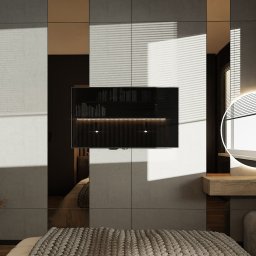 Marlena Pokora - Studio Projektowe - Nowoczesna sypialnia z dużym lustrem, telewizorem wbudowanym w ścianę i toaletką z okrągłym, podświetlanym lustrem, utrzymana w stonowanej kolorystyce z akcentami dekoracyjnymi.