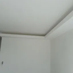 Wnętrze po remoncie z wykończonym sufitem podwieszanym i ścianami pomalowanymi na biało, widoczne ślady po mocowaniach na ścianie.