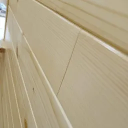 Jasne, świeżo położone drewniane panele ścienne z widocznym usłojeniem i delikatnym połyskiem, ułożone pionowo z minimalnymi odstępami.