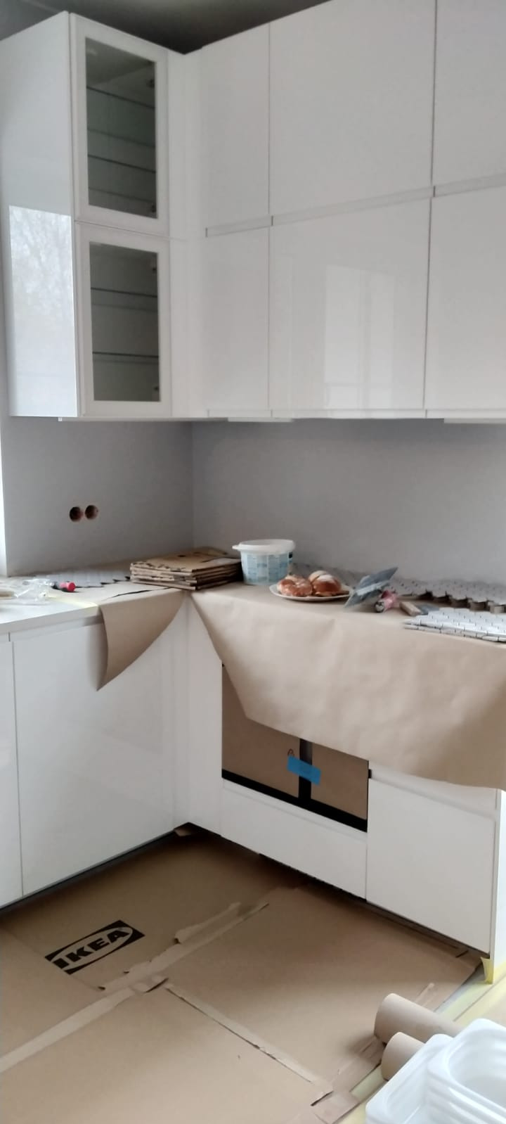 Białe, błyszczące szafki kuchenne IKEA w trakcie montażu w Michałowicach-Wsi, zabezpieczone brązowym papierem, na blacie leżą croissanty.