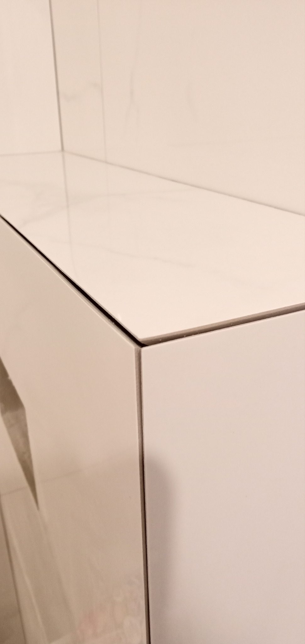 Biała, błyszcząca szafka łazienkowa z blatem z płytek imitujących marmur, widok z bliska na krawędź i połączenie materiałów.